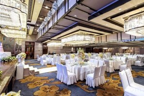 Une salle de banquet avec des tables rondes, des chaises blanches et des lustres.