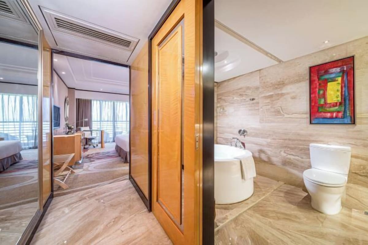 Habitación de hotel con puerta de madera, baño con bañera y retrete, y vista del interior de la habitación.
