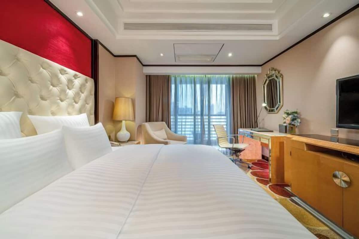 Habitación de hotel con una cama grande, un escritorio, un televisor y vistas a la ciudad.