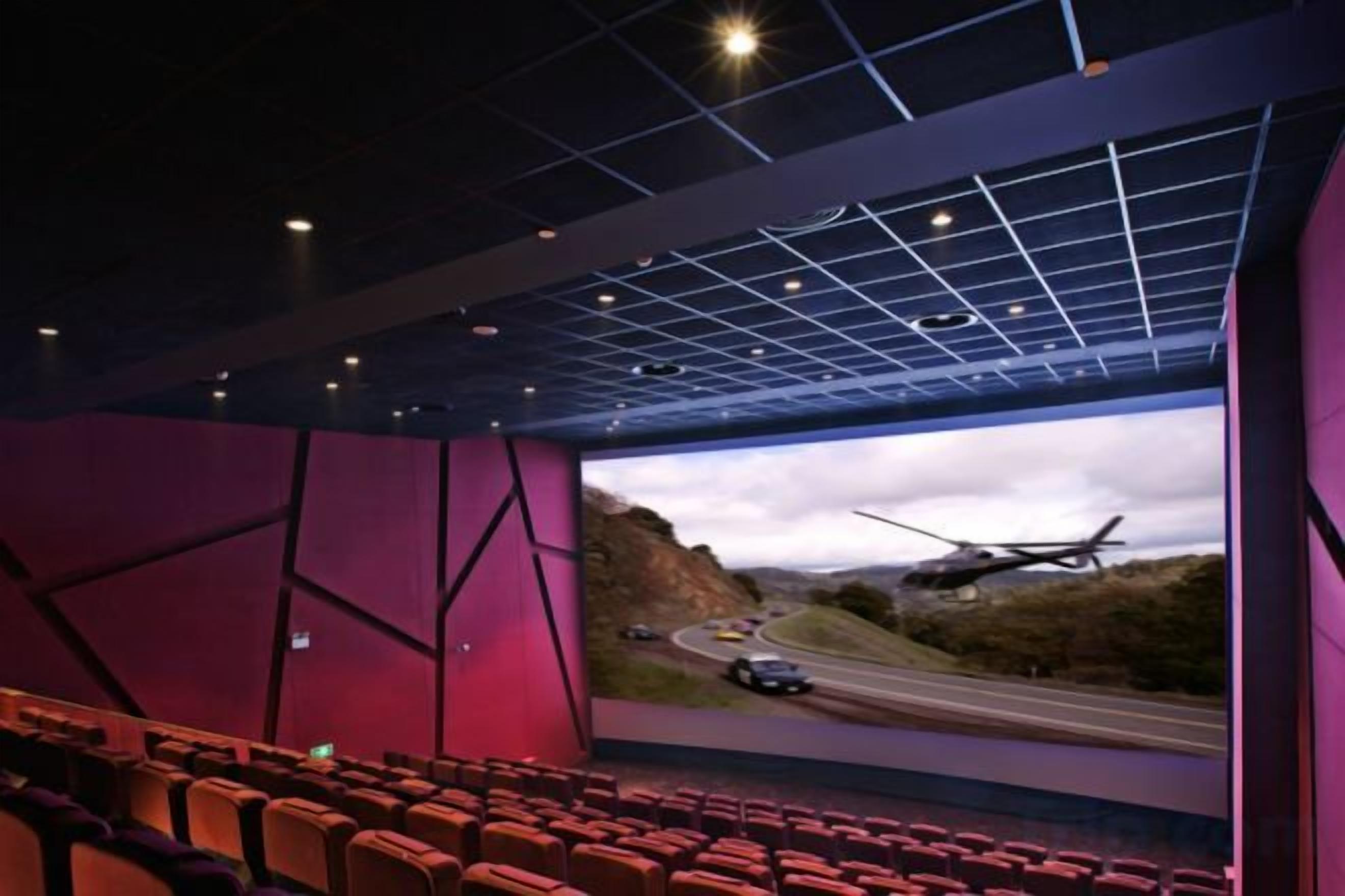 Ein Theater mit Reihen von Sitzplätzen, einer großen Leinwand und einer deckenhohen Rasterstruktur.