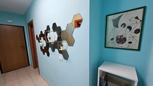 A hallway with a geometric wall decoration, a framed abstract painting, and a white shelf with books. - Southern Comfort Sicily Holidays (Letojanni)