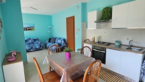 A modern kitchen with white cabinets, a sink, and a stove. There is a dining area with a table and chairs, and a small refrigerator. - Southern Comfort Sicily Holidays (Letojanni)
