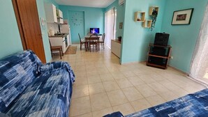 A living room with a sofa, a dining area with a TV, and a kitchen in the background. - Southern Comfort Sicily Holidays (Letojanni)