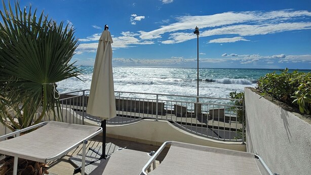 Een balkon met uitzicht op de oceaan, voorzien van ligbedden en een strandparasol.