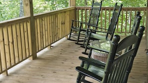 A wooden deck with a row of green rocking chairs and a glass table.