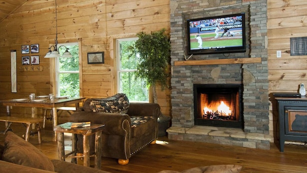 A cozy cabin interior with a stone fireplace, a television mounted above it, and a ceiling fan.