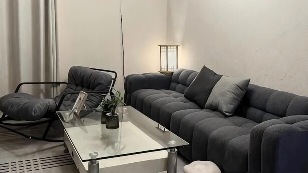 A modern living room with a glass coffee table, a grey sofa, a black chair, and a floor lamp. - Reverse Time Youth Hostel (Nanjing Station South Square Branch) (Nanjing)