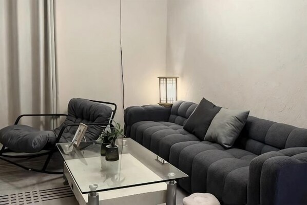 A modern living room with a glass coffee table, a grey sofa, a black chair, and a floor lamp.