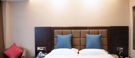 Ein Hotelzimmer mit einem großen Bett, einem braunen Kopfteil, einem roten Kissen, einem Nachttisch mit Telefon und einer Wandleuchte.