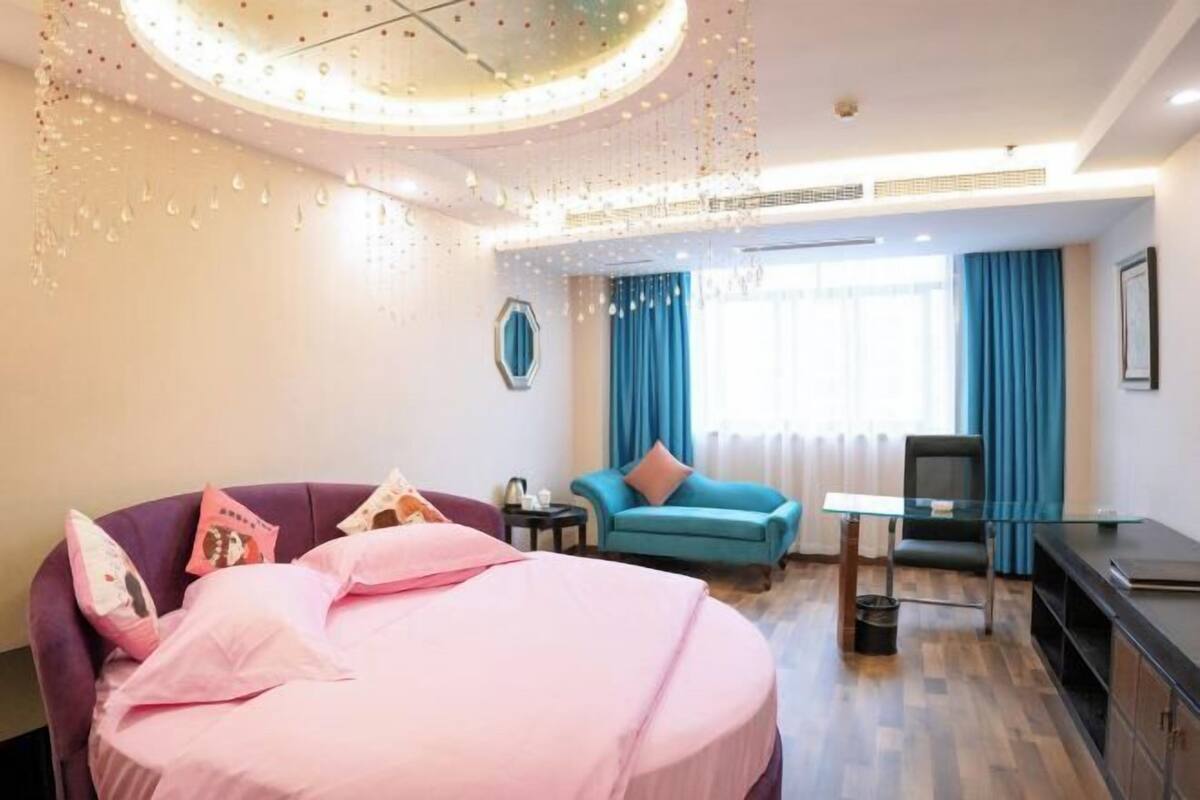 Una habitación de hotel con una cama, un sillón azul, una mesa de vidrio y un escritorio.