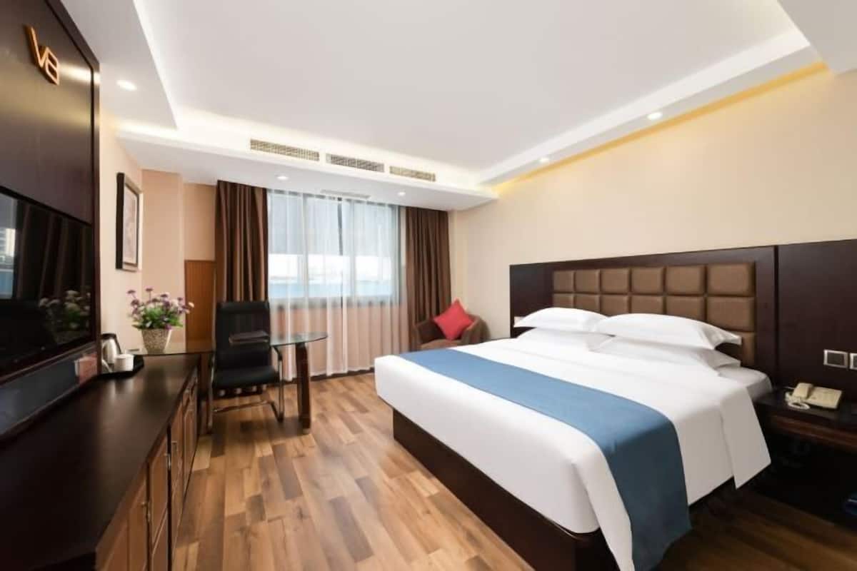 Habitación de hotel con cama, escritorio, silla, televisión y ventana con cortinas.