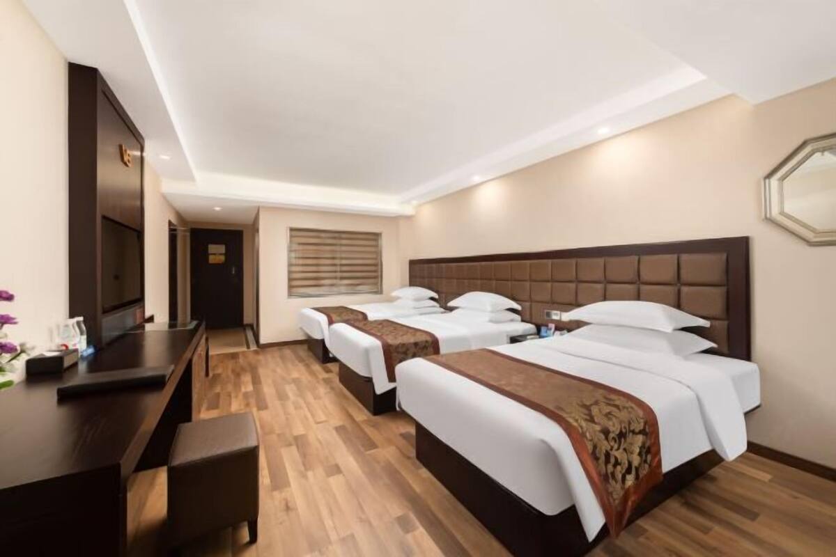 Habitación de hotel con tres camas, un escritorio y televisor de pantalla plana, y suelo de madera.
