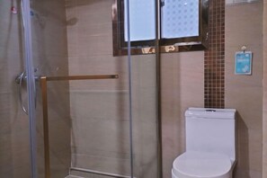 Een badkamer met een douchecabine van glas, een wit toilet en een betegelde muur met een klein poster.
