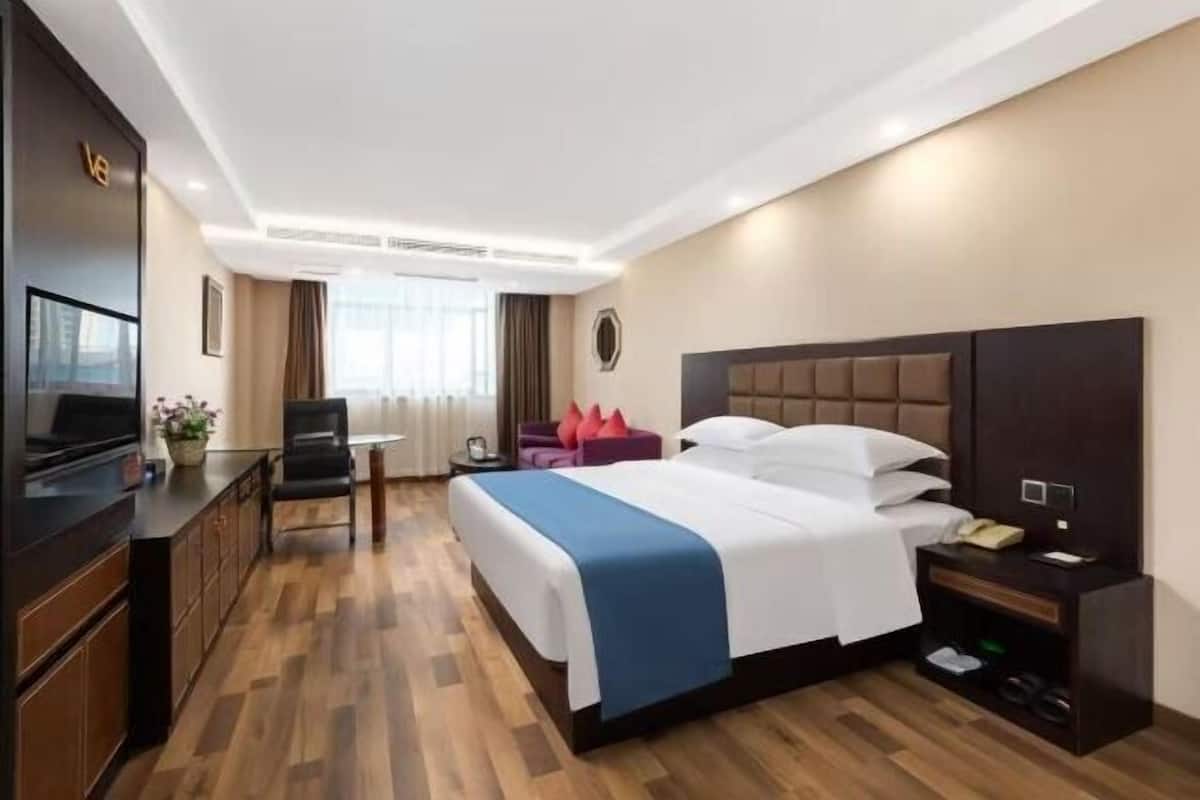 Habitación de hotel con cama, mesita de noche, televisor, escritorio, silla y vistas al exterior.