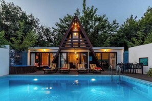 A modern building with a triangular roof structure, a swimming pool, and lounge chairs. - a sultan 1

 (Kas)