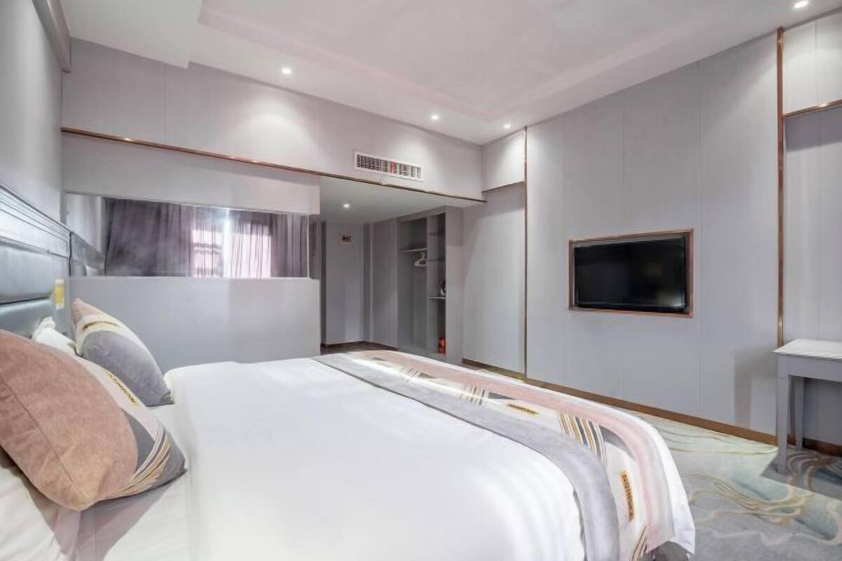 A modern hotel room with a large bed, a TV mounted on the wall, and a walk-in closet.