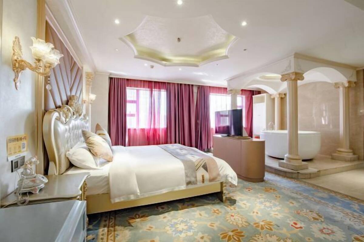 A spacious bedroom with a large bed, a vanity, a bathtub, and a ceiling with a unique design.
