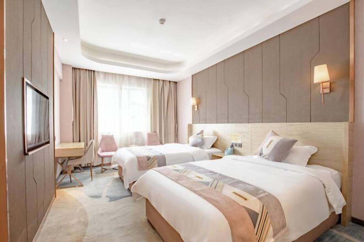 A hotel room with two beds, a desk, and a TV.