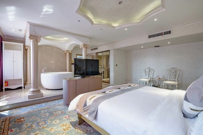 A spacious hotel room with a large bed, a bathtub, a television, and a seating area with chairs.