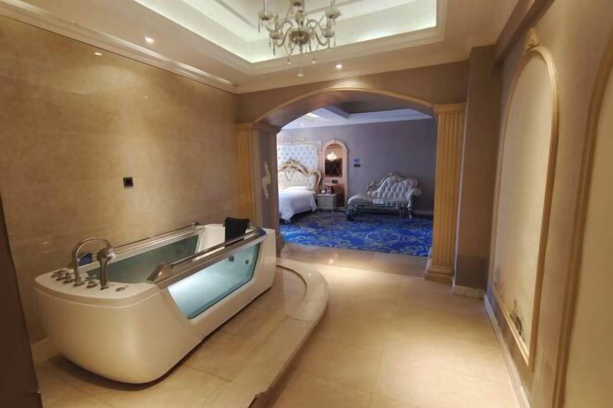 A luxurious bathroom with a modern bathtub, a mirror, and a bed in the adjacent room.
