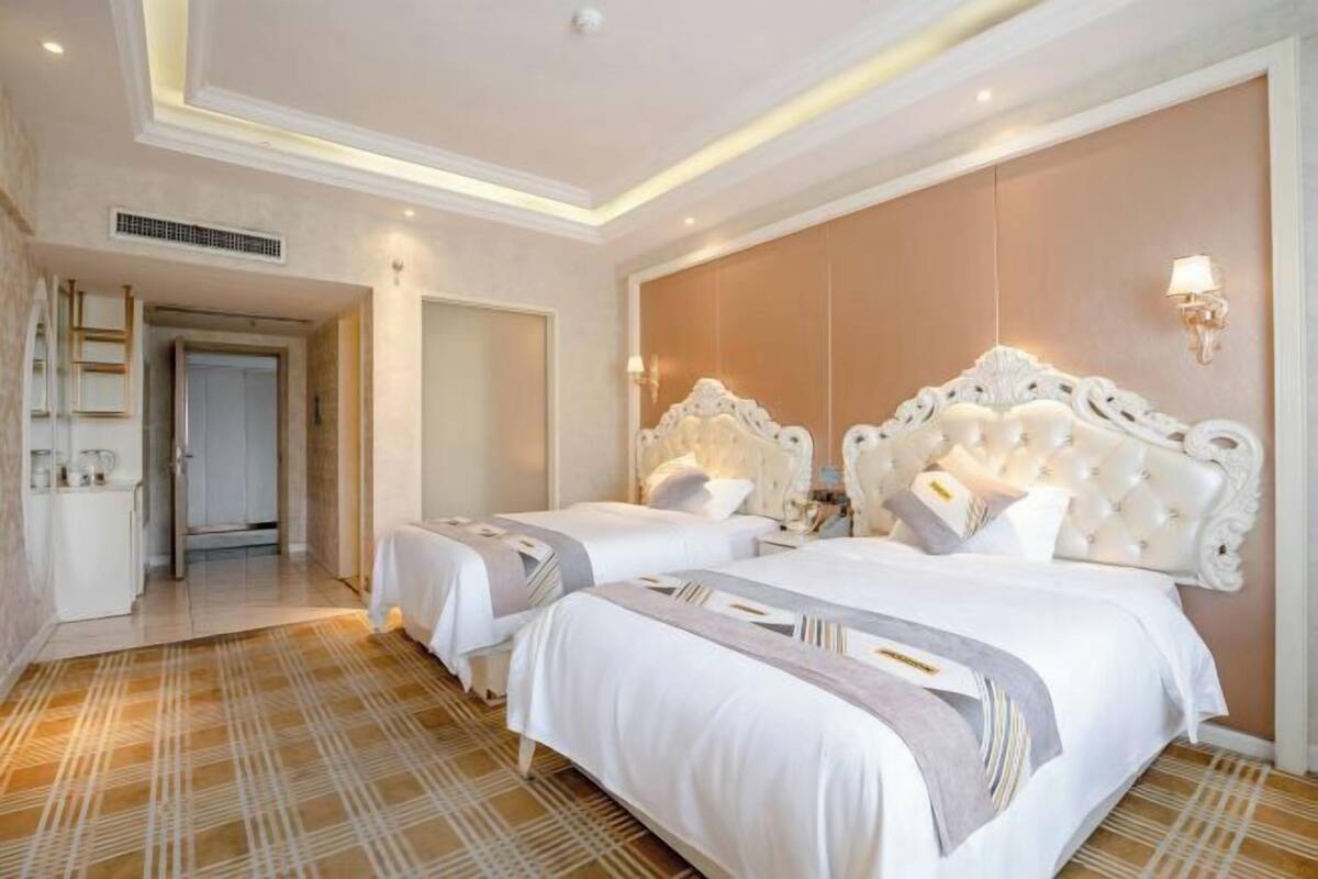 A hotel room with two beds, a large mirror, a wardrobe, and a bathroom with a shower and toilet.