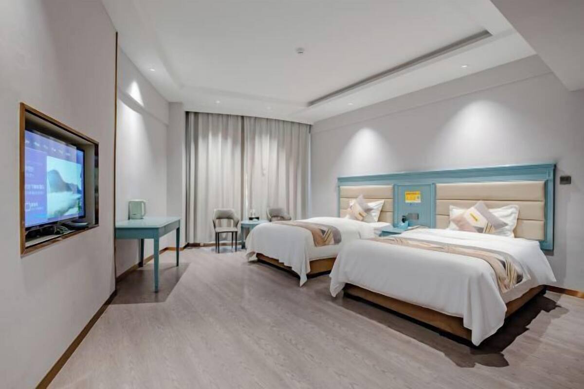 A hotel room with two beds, a desk, a TV, and a window with curtains.