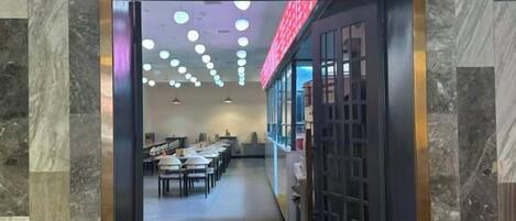 Vista del interior de un comedor con mesas y sillas, un techo con luces circulares y un separador de vidrio con diseño de cuadrícula.