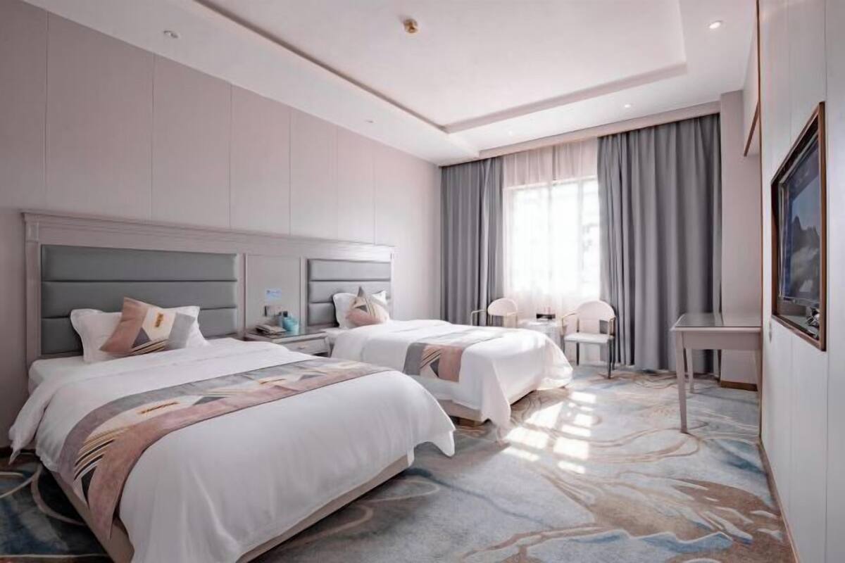 A hotel room with two beds, a desk, a chair, and a large window with curtains.
