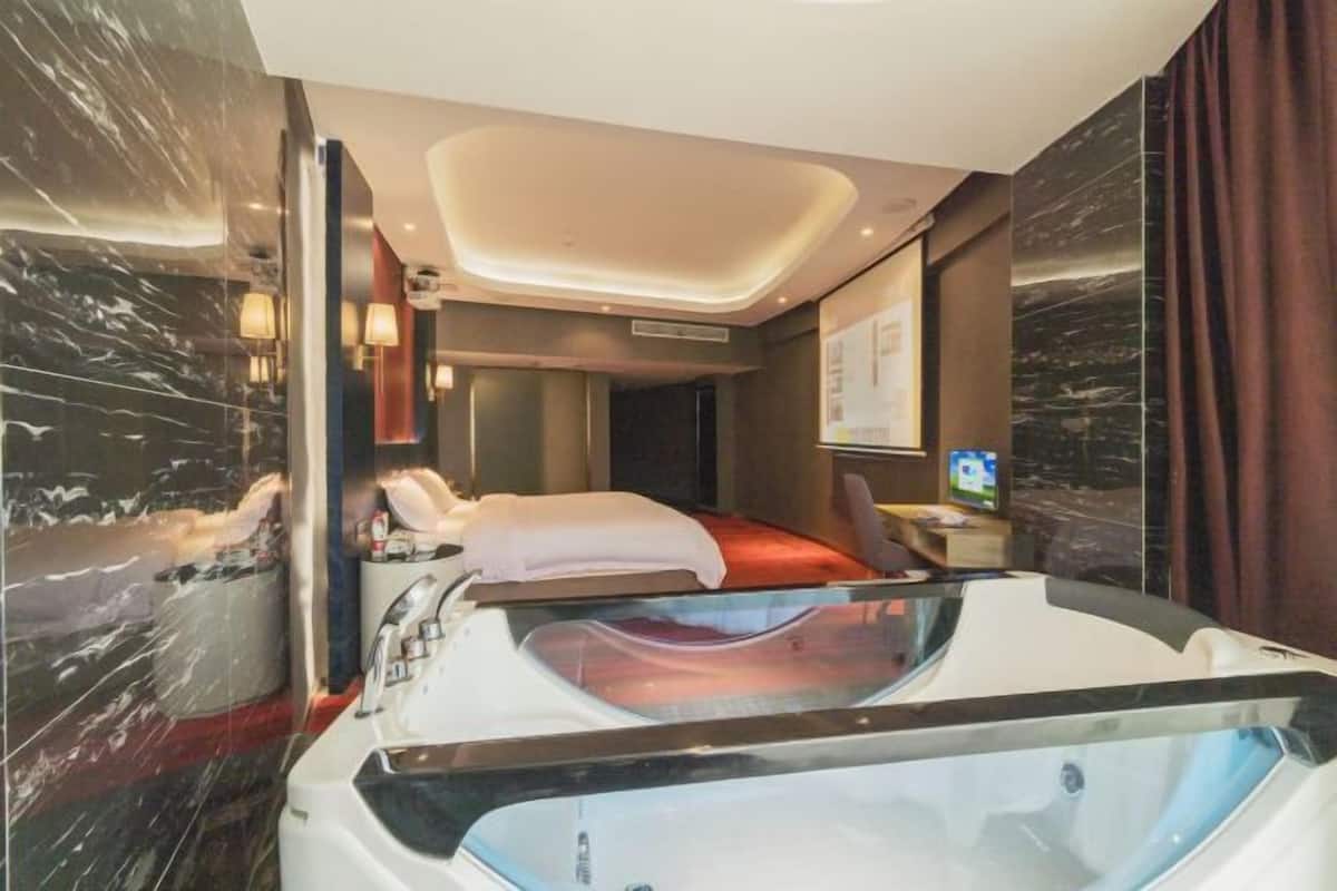 A modern hotel room with a large bathtub, a bed, and a television on a bedside table.