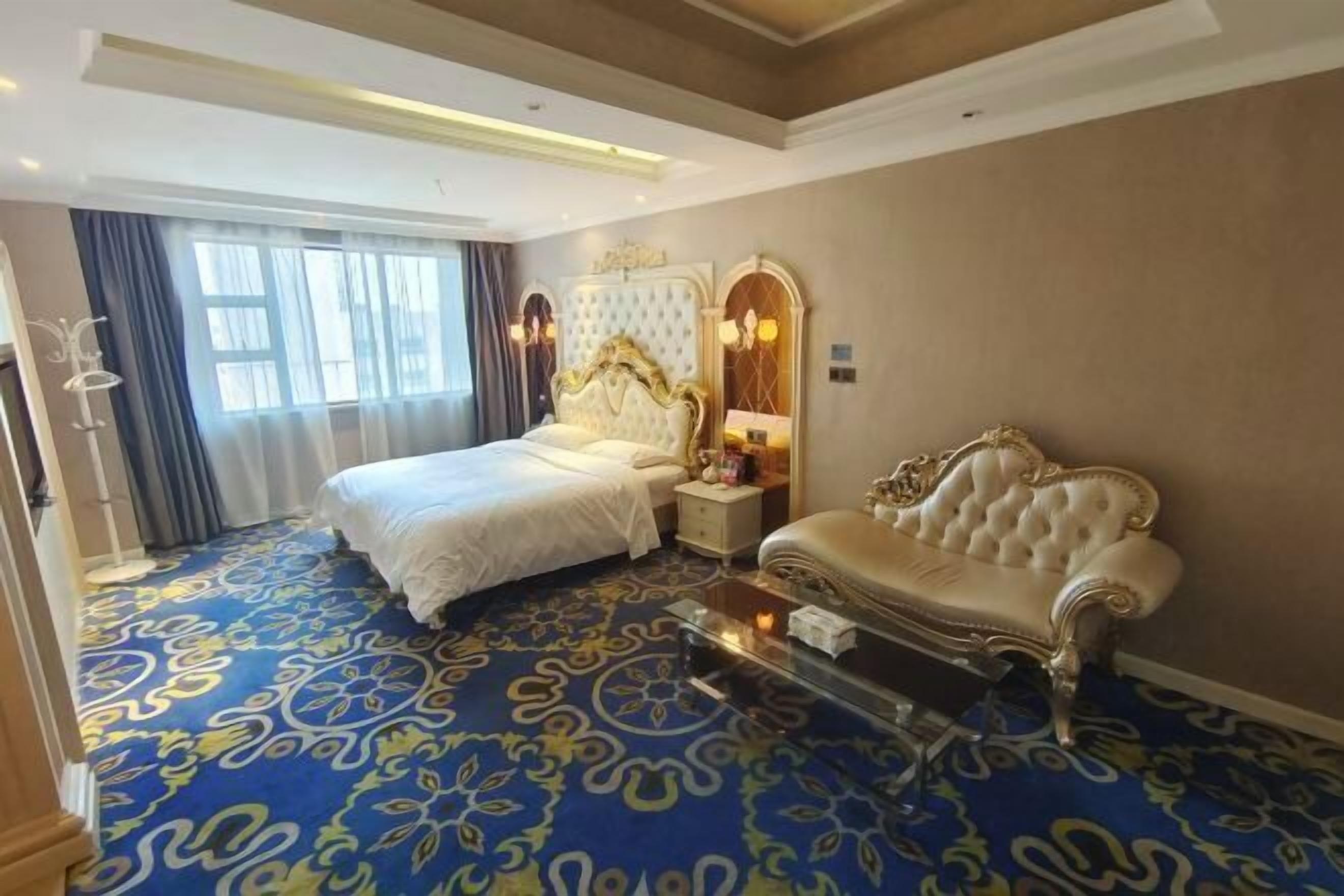 A hotel room with a large bed, a sofa, a glass coffee table, and a decorative mirror.