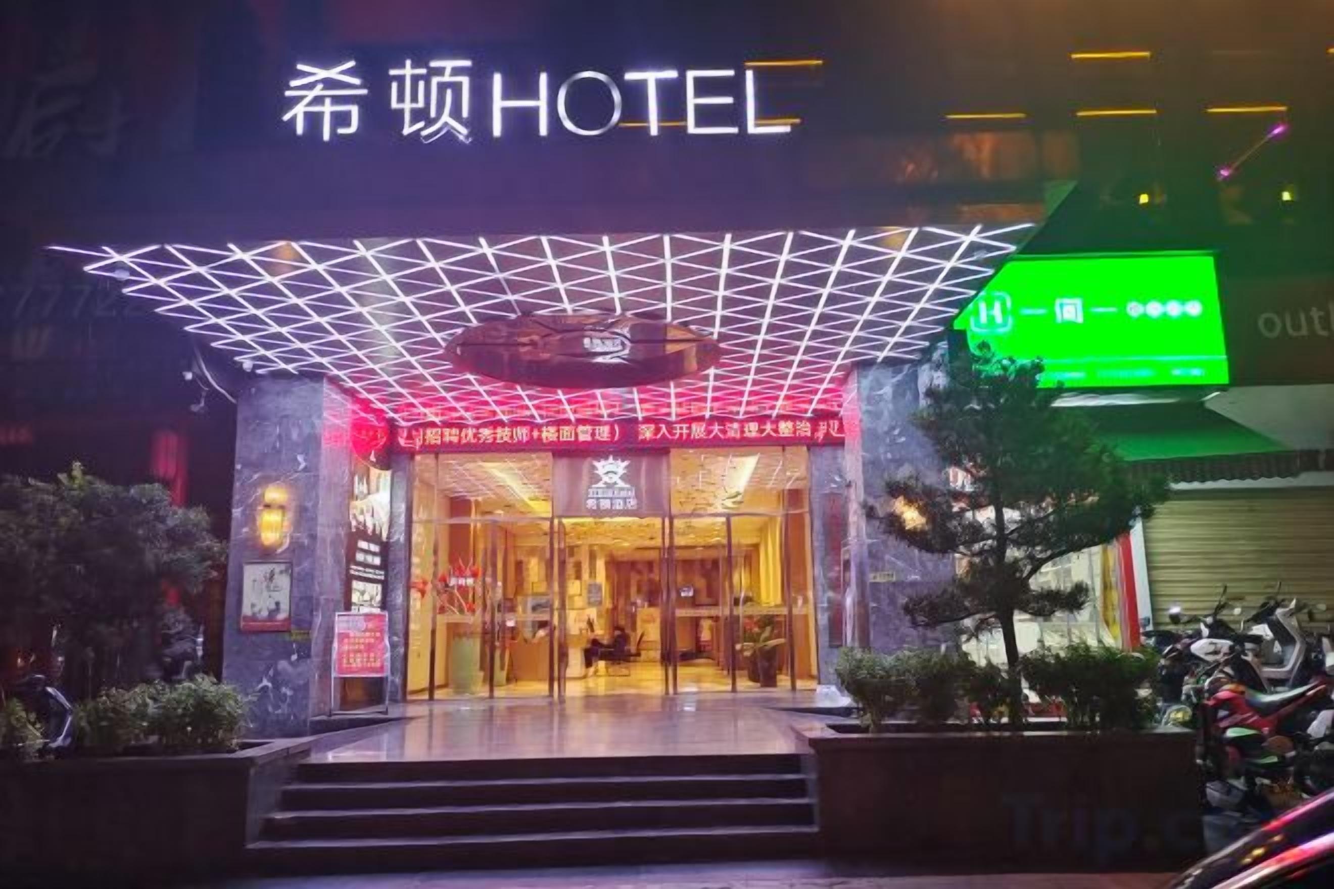 The entrance of a hotel with a modern design, featuring a glass facade and a geometric roof structure.