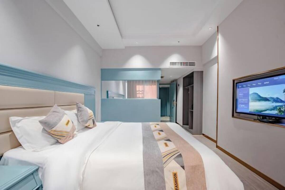 A modern hotel room with a large bed, a TV on the wall, and a desk with a chair.