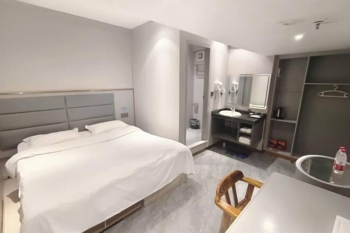A modern hotel room with a large bed, a bedside table, a mirror, a small desk, and a chair.