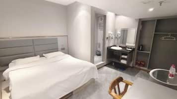 A modern hotel room with a large bed, a bedside table, a mirror, a small desk, and a chair.