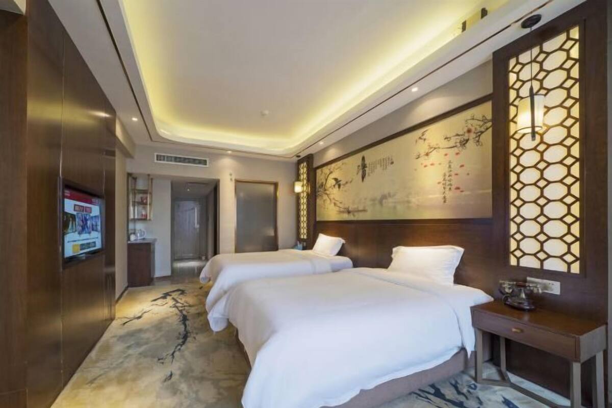 A hotel room with two beds, a wooden headboard, a wall-mounted artwork, and a television.