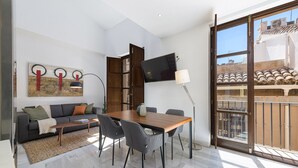 A modern living room with a sofa, coffee table, dining table, and chairs. A flat-screen TV is mounted on the wall, and a lamp is on a side table. - Solaga - Pozos Dulces (Málaga)