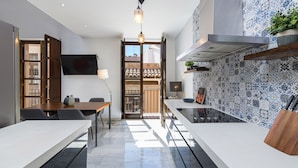 A modern kitchen with a dining area, a TV mounted on the wall, and a balcony with a view. - Solaga - Pozos Dulces (Málaga)