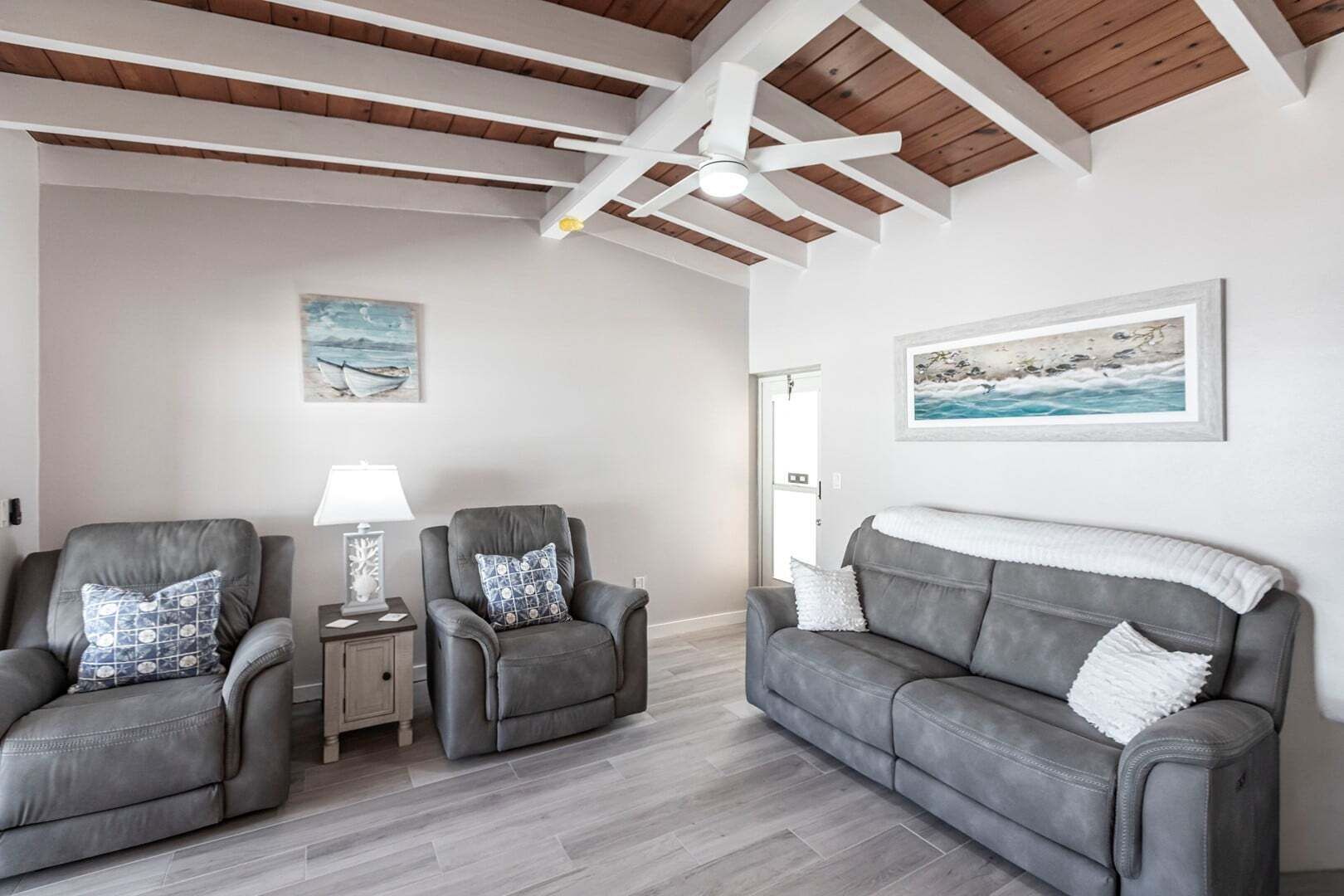 A living room with two leather armchairs, a grey sofa, a small table with a lamp, and artwork on the walls.