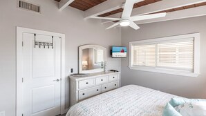 A bedroom with a bed, dresser, vanity, ceiling fan, and a TV mounted on the wall. - 65 Standard - Island Vibes - Your Perfect One-Bedroom Villa in Siesta Key Awaits (Siesta Key)
