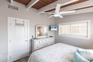 Une chambre à coucher comprenant un lit, une commode, une coiffeuse, un ventilateur de plafond et un téléviseur fixé au mur.