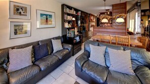 A living room with two leather sofas, a bookshelf, and a dining area with wooden furniture. - Meters from the lift station with a private terrace and balcony in Verbier (Val de Bagnes)