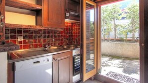 A kitchen with wooden cabinets, a tiled backsplash, a dishwasher, and a window with a view of the street. - Meters from the lift station with a private terrace and balcony in Verbier (Val de Bagnes)
