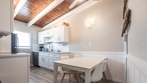 A compact kitchen with white cabinetry, a dining table with chairs, and a wooden ceiling.