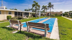 Ein Poolbereich mit blauem Pool, zwei Bänken und Palmen.