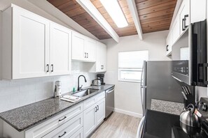 Una cocina moderna con armarios blancos, encimera de granito, refrigerador de acero inoxidable y tetera.