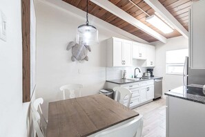 A modern kitchen with white cabinets, a wooden dining table, and a hanging light fixture. - 63 Premium - Dreamy Siesta Key - Unwind in a Stylish One-Bedroom Villa (Siesta Key)