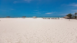 Ein Strand mit weißem Sand, blauem Himmel und mehreren Strandkörben.