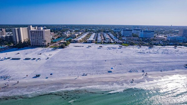 A beach with rows of beach chairs and umbrellas, a clear sky, and buildings in the background.