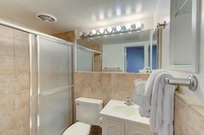 Een badkamer met douche, toilet, wastafel en een spiegel met verlichting erboven.