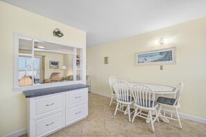 A dining area with a white table and chairs, a white cabinet with drawers, a large mirror, and a framed picture on the wall.
